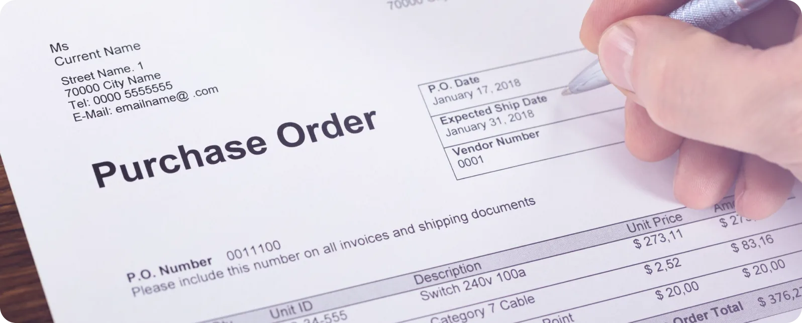Purchase order document being held, showing vendor details, P.O. date January 17 2018, and line items with pricing